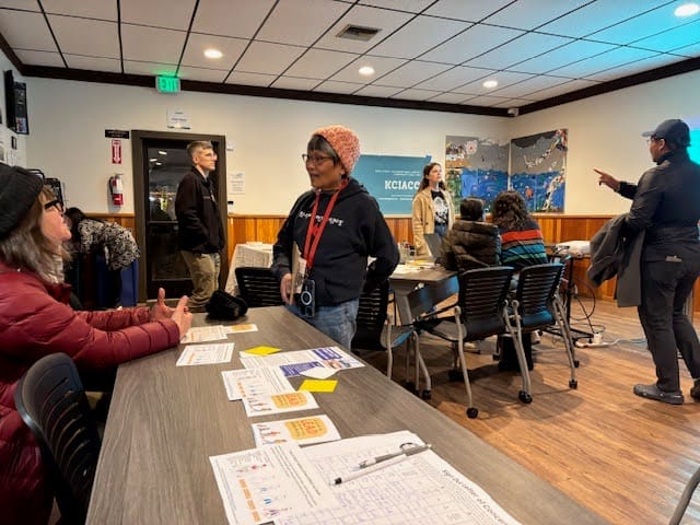 Organisers at a community organising event. The photo shows a hall with people stood and sat around tables chatting.